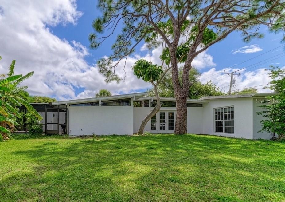 The exterior of a white mid-century modern house features a large tree and lawn — 315 PARK BOULEVARD S, VENICE, FL