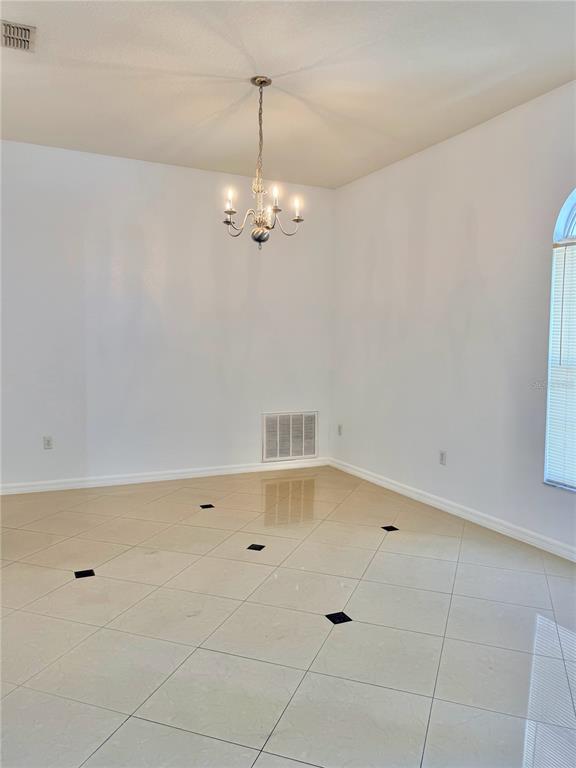 An empty dining room features white walls, a chandelier, and light tile flooring with black accents — 6759 KRENSON OAKS CIRCLE, LAKELAND, FL