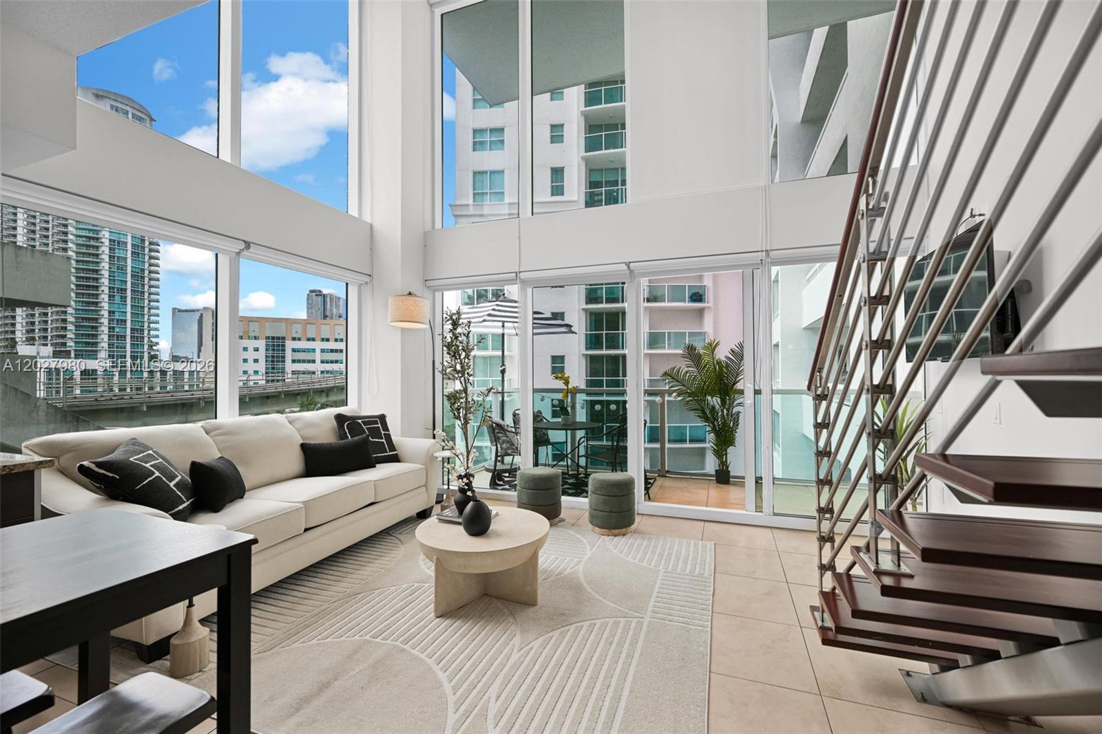 A modern living room features floor-to-ceiling windows, a white sofa, and a floating staircase — 41 SE 5th St # 517, Miami FL 33131, MIAMI, FL