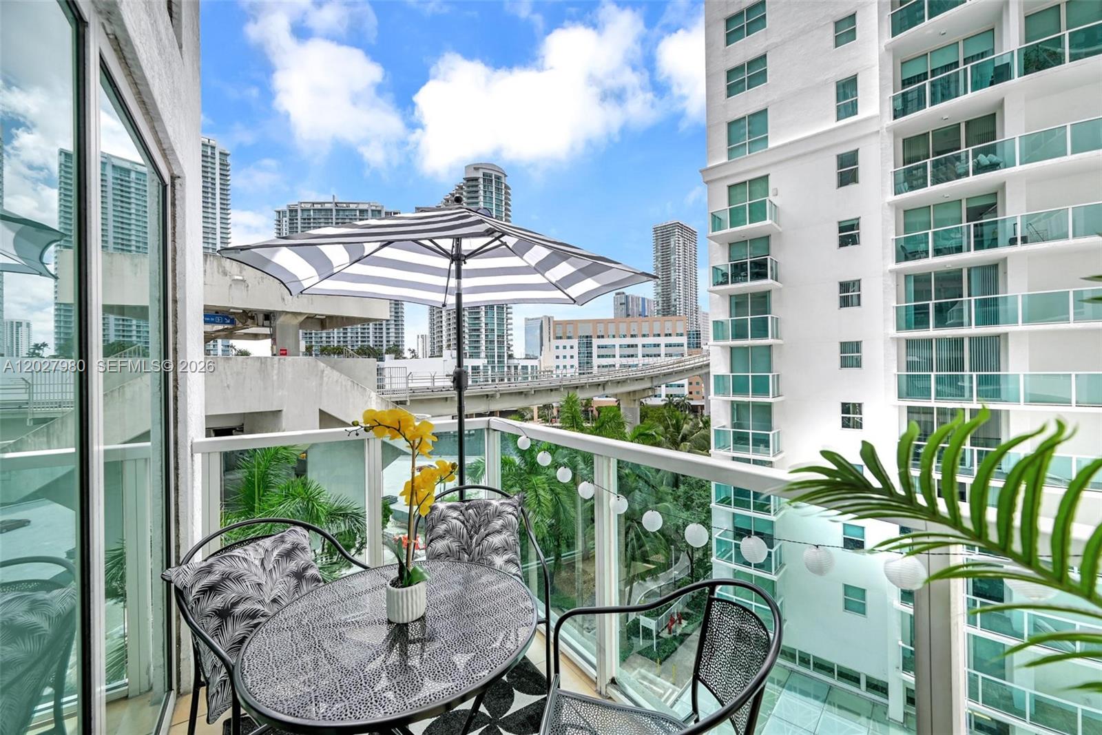 A balcony features a small table, chairs, a striped umbrella, and views of city buildings — 41 SE 5th St # 517, Miami FL 33131, MIAMI, FL