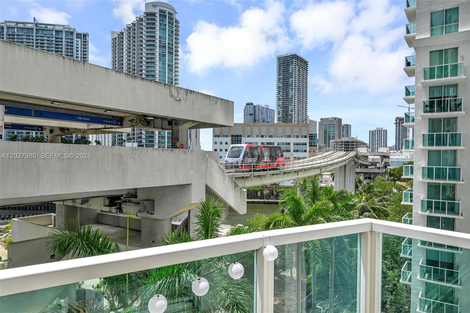 A balcony view shows the Miami Metromover train passing by high-rise buildings and palm trees — 41 SE 5th St # 517, Miami FL 33131, MIAMI, FL