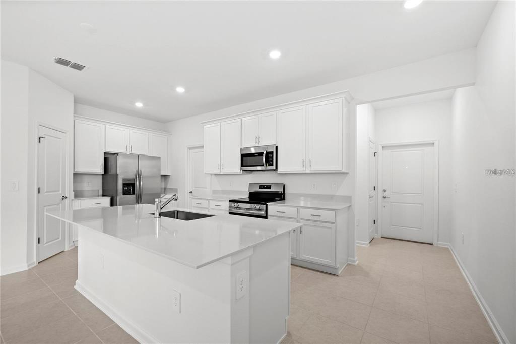 A modern kitchen features white cabinetry, stainless steel appliances, a center island, and tile flooring — 6028 ZEN WAY, CLERMONT, FL