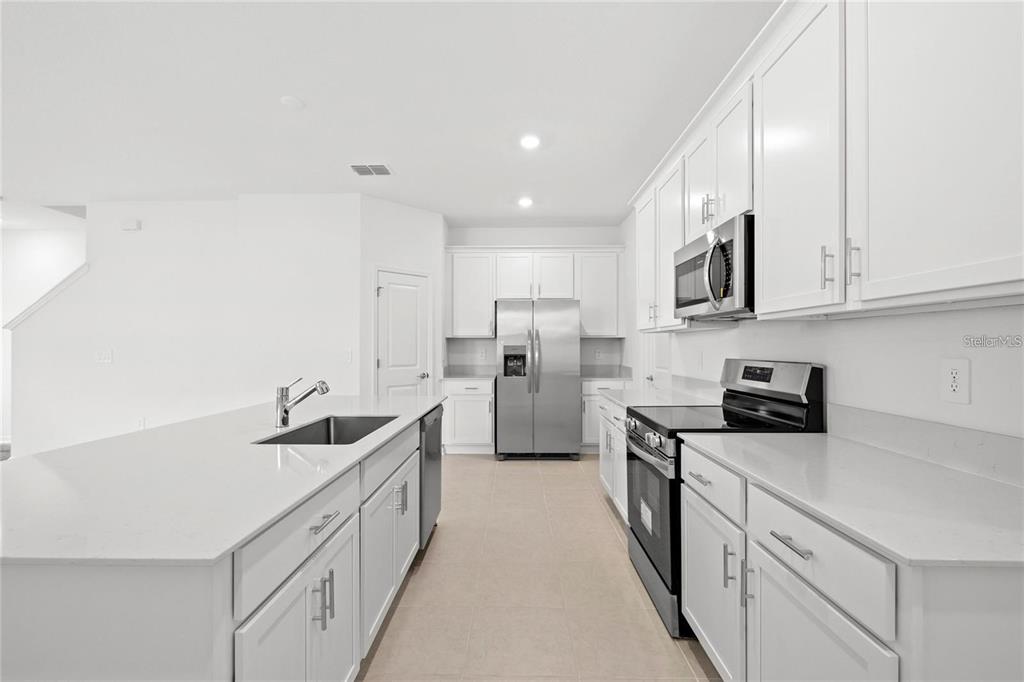 A modern kitchen features white cabinets, stainless steel appliances, and a large quartz-topped island — 6028 ZEN WAY, CLERMONT, FL