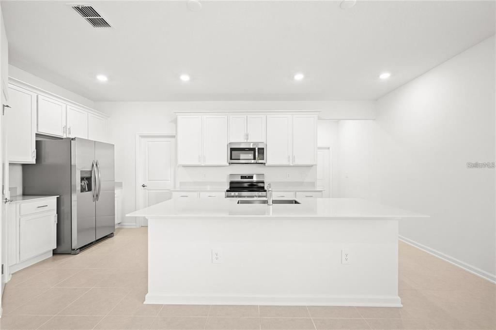 A modern white kitchen features stainless steel appliances, a large center island, and tile flooring — 6028 ZEN WAY, CLERMONT, FL