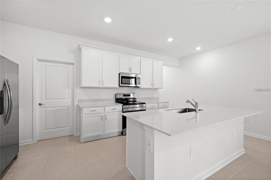 A modern kitchen features white cabinetry, stainless steel appliances, and a central quartz island — 6028 ZEN WAY, CLERMONT, FL