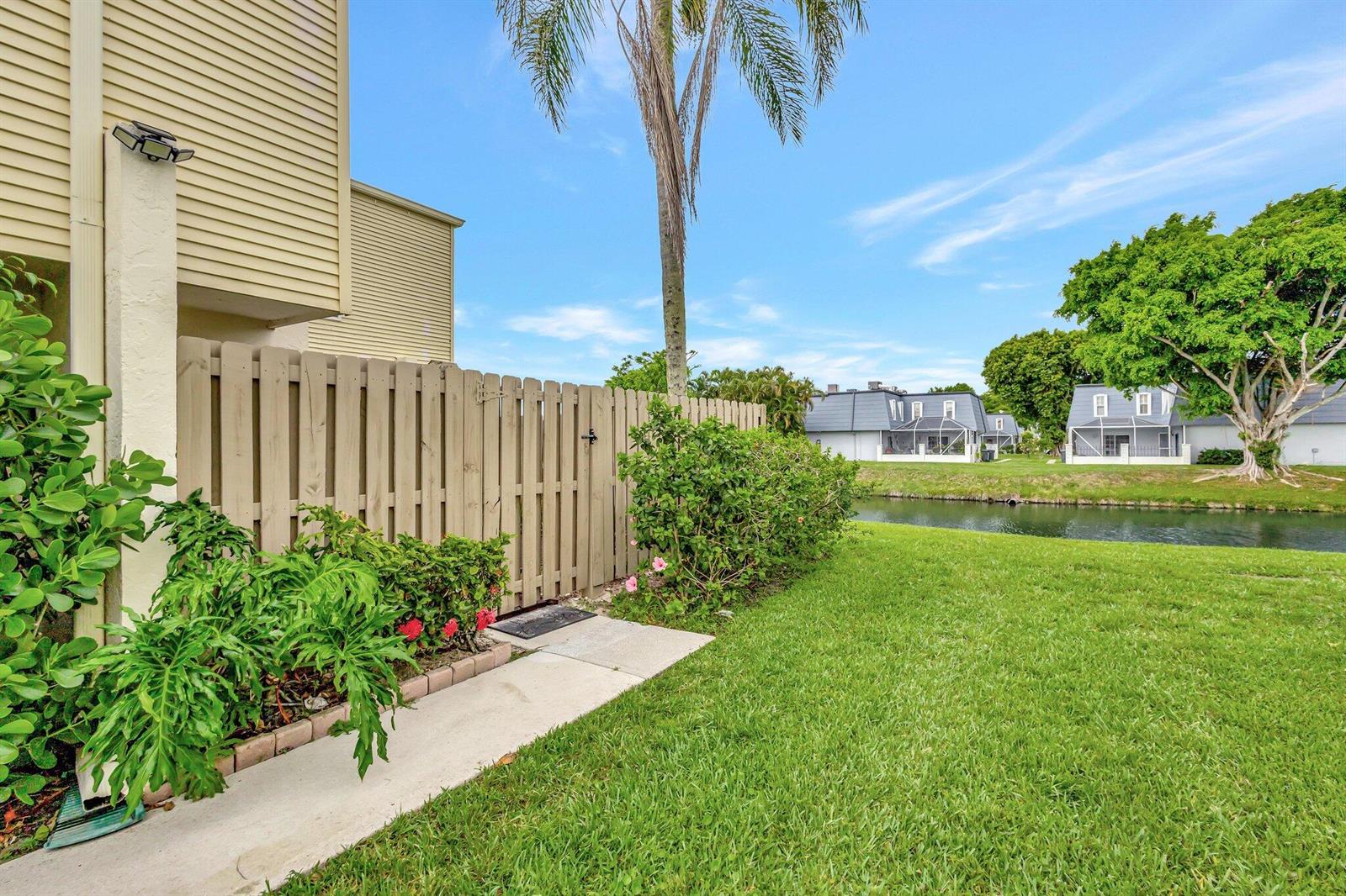 A wooden fence borders a grassy yard next to a canal with houses in the background — 1586 Shaker Circle, Wellington FL 33414, WELLINGTON, FL