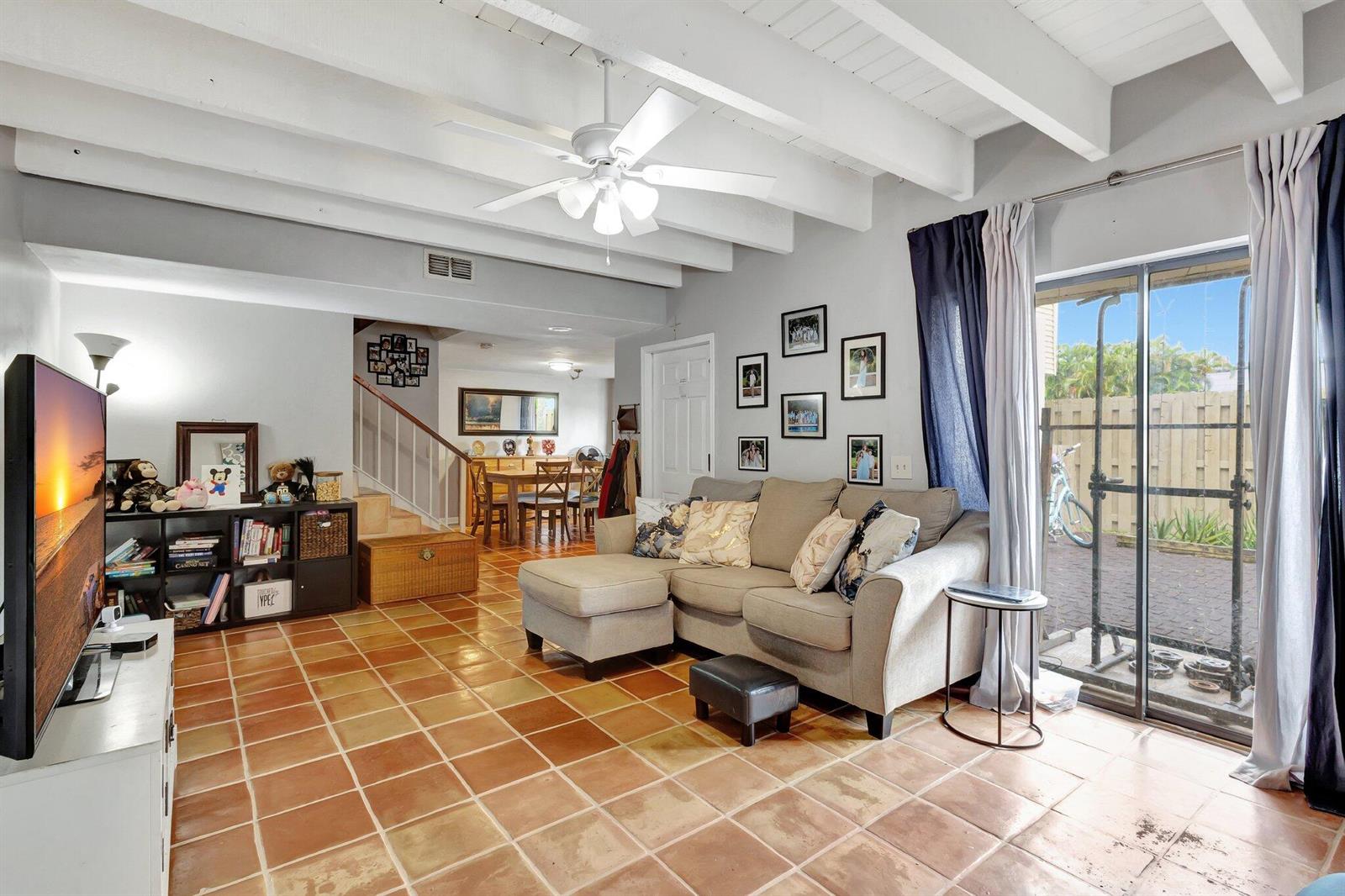 A living room with terracotta tile floors, a sectional sofa, and exposed white ceiling beams — 1586 Shaker Circle, Wellington FL 33414, WELLINGTON, FL