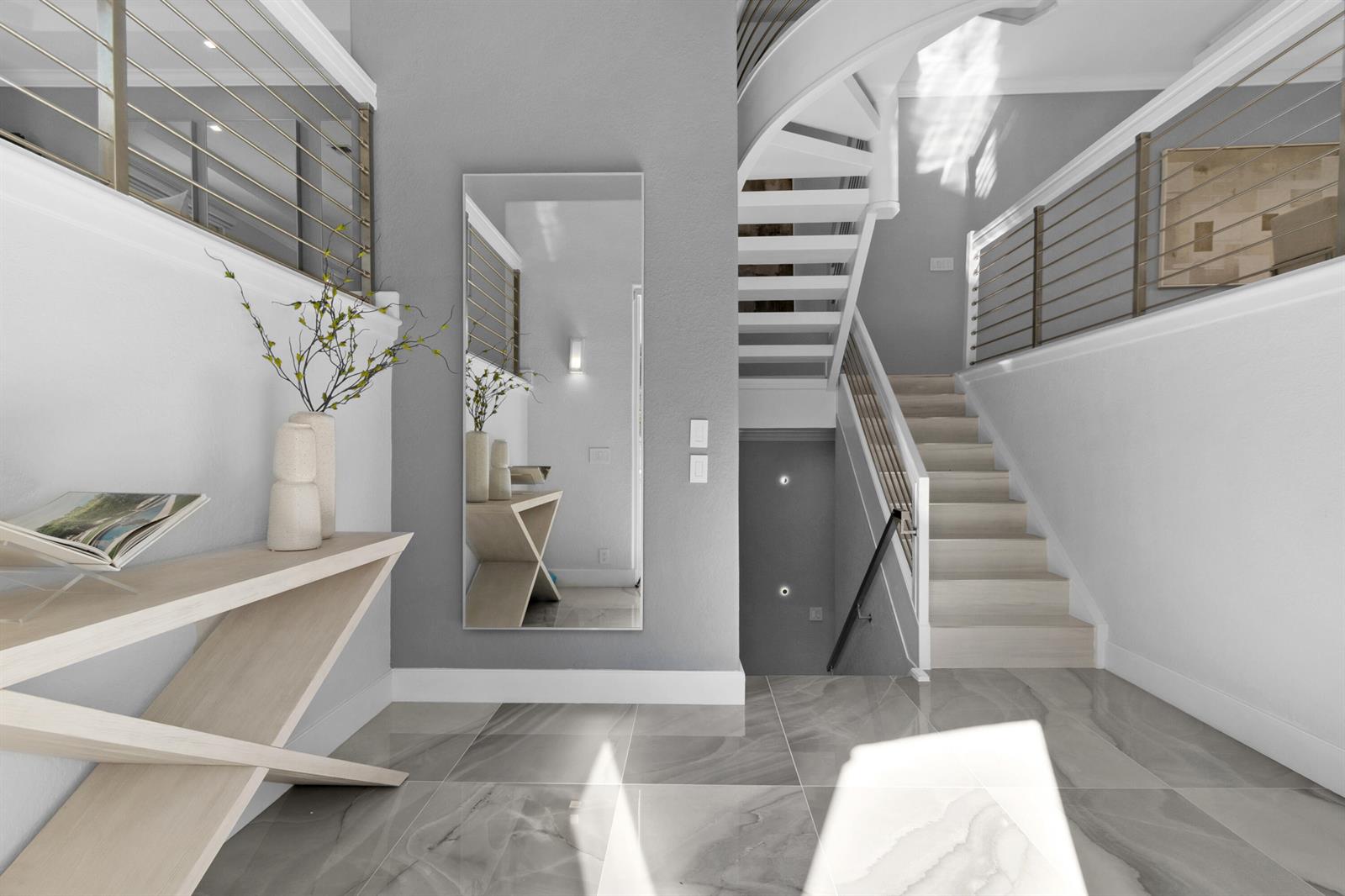 A modern entryway features a light wood console table, a tall mirror, and a staircase — 1792 Bay Drive # 27, Pompano Beach FL 33062, POMPANO BEACH, FL