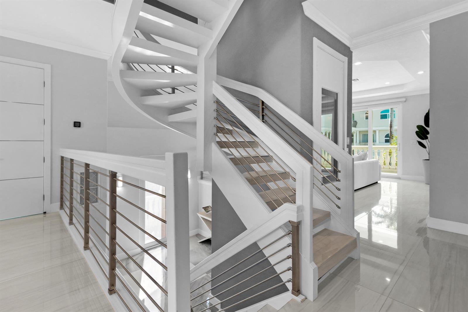 A modern staircase with white railings and metal cables sits in a bright, tiled hallway — 1792 Bay Drive # 27, Pompano Beach FL 33062, POMPANO BEACH, FL