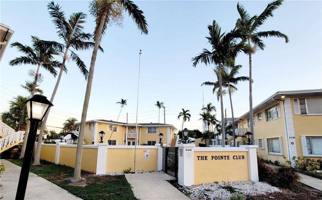 The exterior of a yellow apartment complex features palm trees and a gated entrance sign — FORT LAUDERDALE, FL