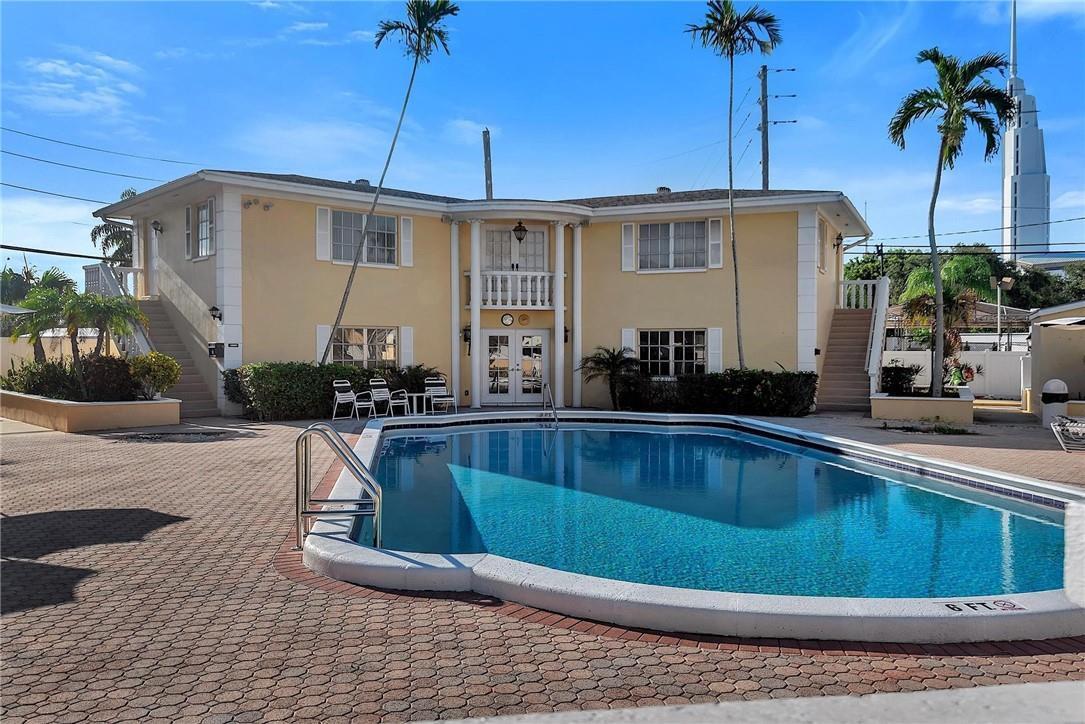 A two-story yellow building with a swimming pool and palm trees in the foreground — FORT LAUDERDALE, FL