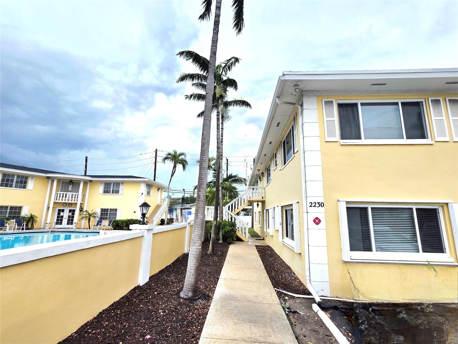A yellow two-story apartment building with a swimming pool and palm trees — FORT LAUDERDALE, FL