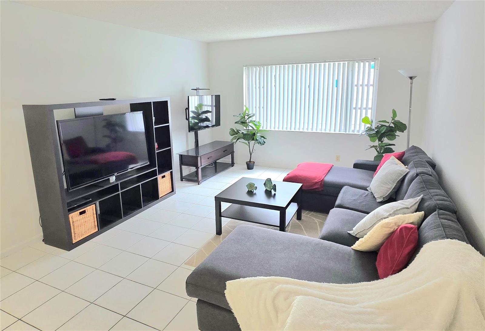 A living room features a large sectional sofa, a television unit, and white tile flooring — FORT LAUDERDALE, FL