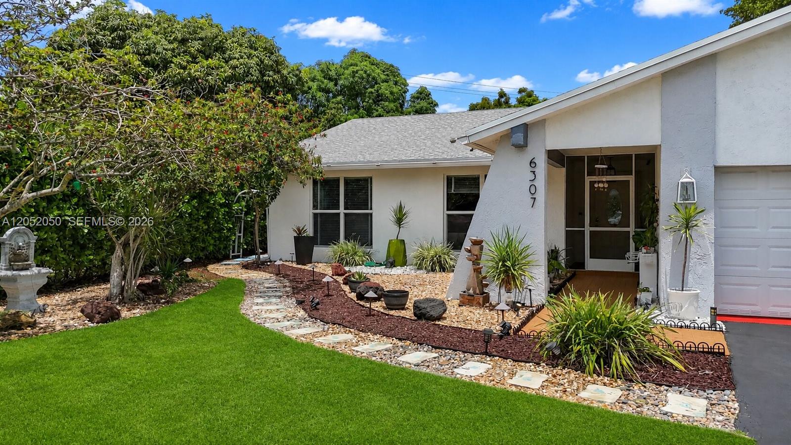 A single-story house features a white stucco exterior, a stone walkway, and landscaped garden beds — 6307 Silk Oak Cir, Tamarac FL 33319, TAMARAC, FL