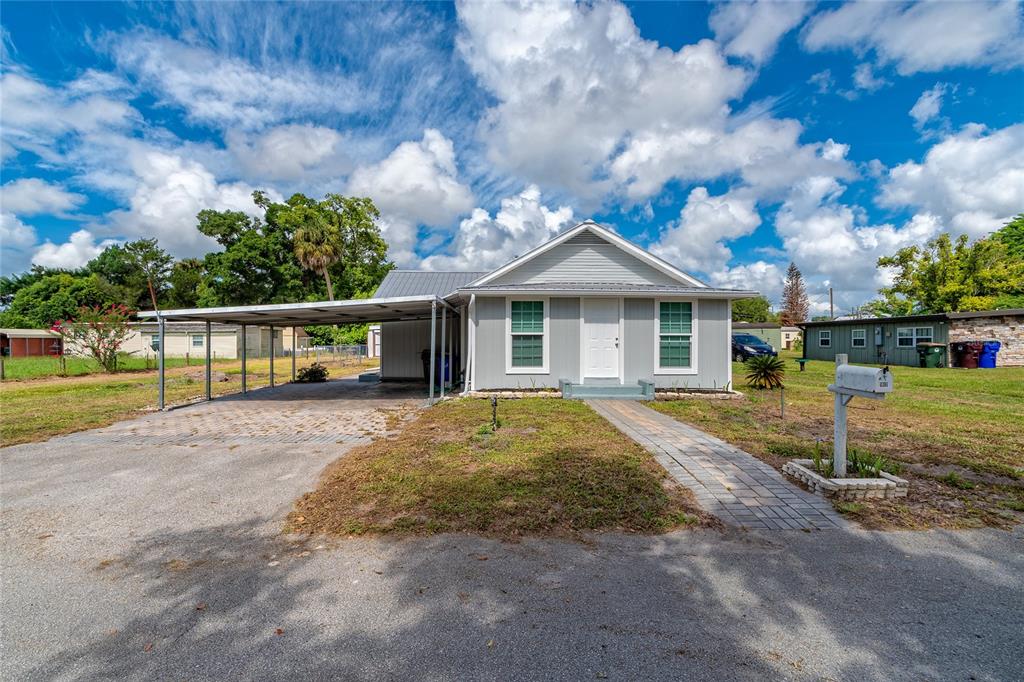 A light gray single-story house features a metal roof, a carport, and a paved walkway — 1812 KENTUCKY AVENUE, ST CLOUD, FL