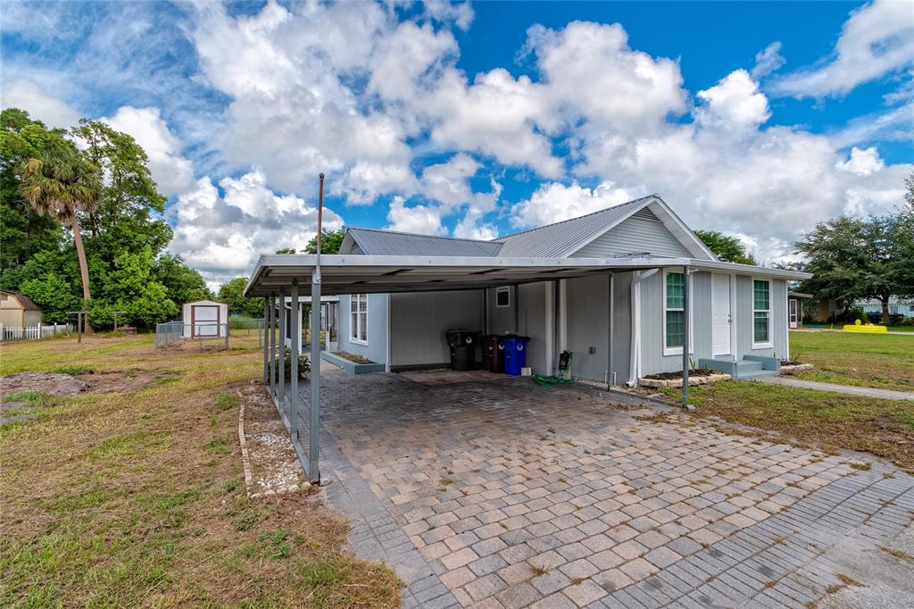 A single-story house with a metal roof, a paved carport, and a small storage shed — 1812 KENTUCKY AVENUE, ST CLOUD, FL