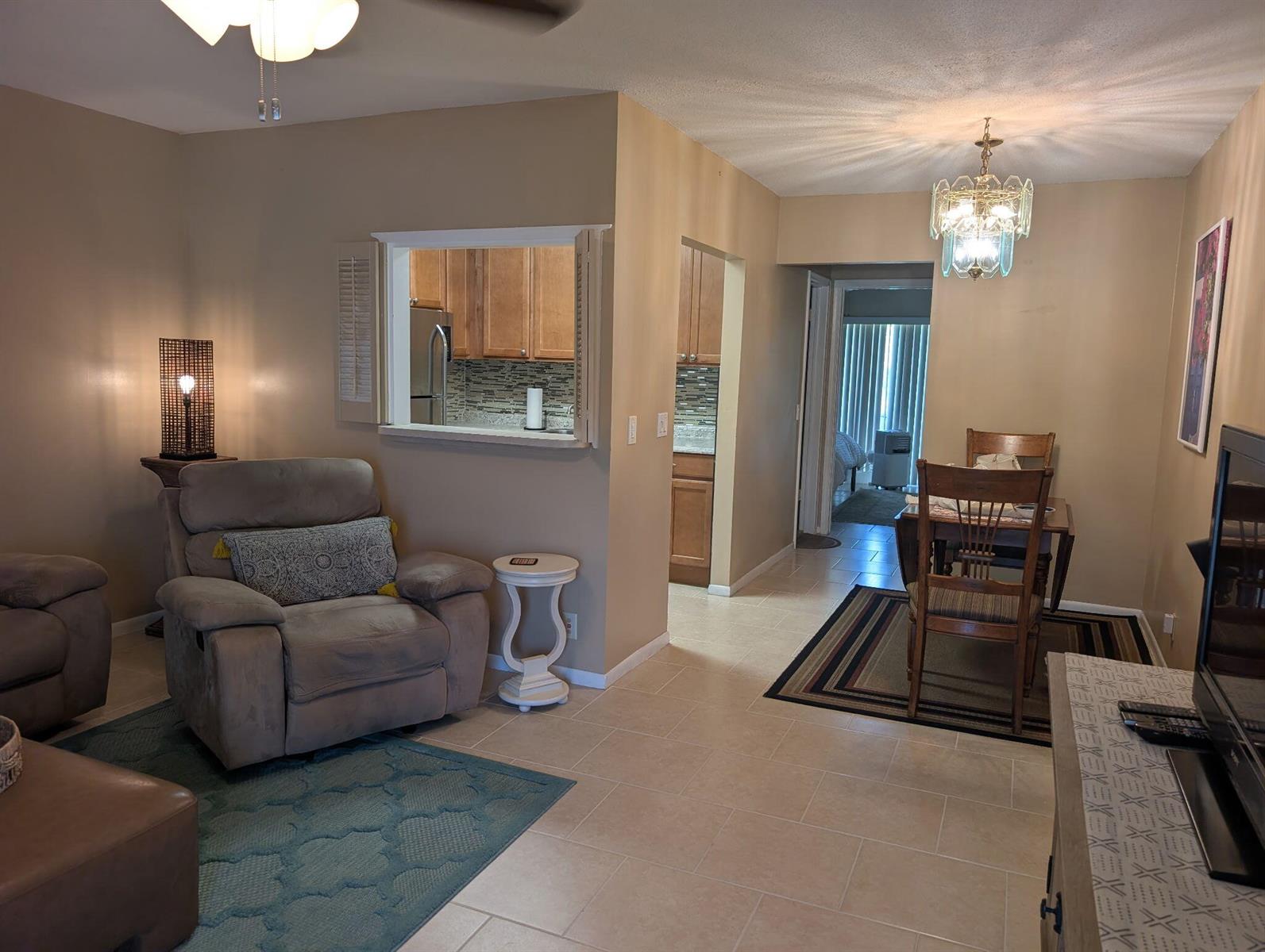 A living room with tile floors, a pass-through window to the kitchen, and dining area — 190 Easthampton H, West Palm Beach FL 33417, WEST PALM BEACH, FL