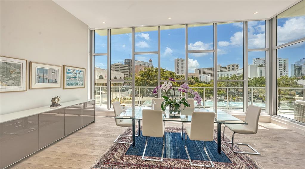 A dining room features a glass table, modern chairs, and floor-to-ceiling windows overlooking a city — 1335 2ND STREET UNIT Villa 2E, SARASOTA, FL