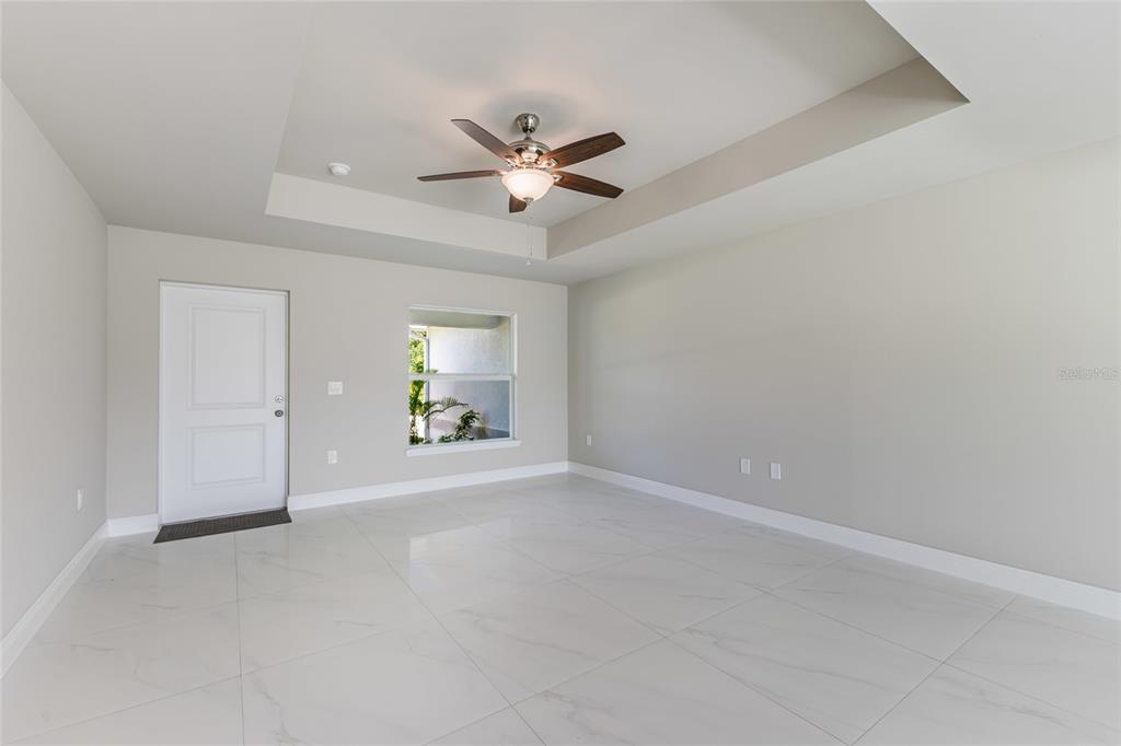 An empty room features white tile flooring, a tray ceiling with a fan, and a door — 1964 LEGHORN STREET, LEHIGH ACRES, FL