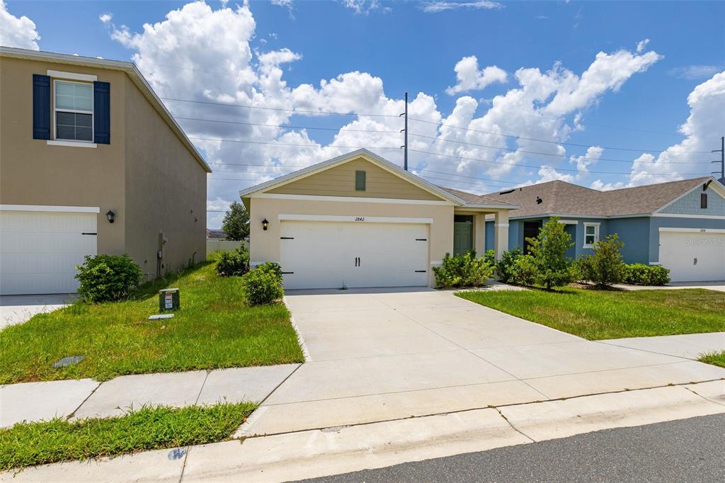 A single-story suburban house with a white garage door and a concrete driveway — 2842 WATERLILY WAY, KISSIMMEE, FL