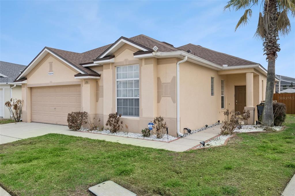 A single-story tan stucco house with a two-car garage and a front walkway — 170 BLOOMINGDALE DRIVE, DAVENPORT, FL