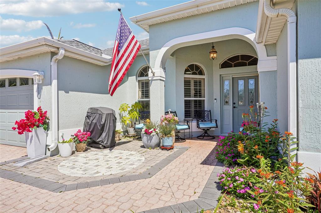 A light blue house exterior features a paved patio, a front door, and potted flowers — 2837 GRANT WAY, THE VILLAGES, FL