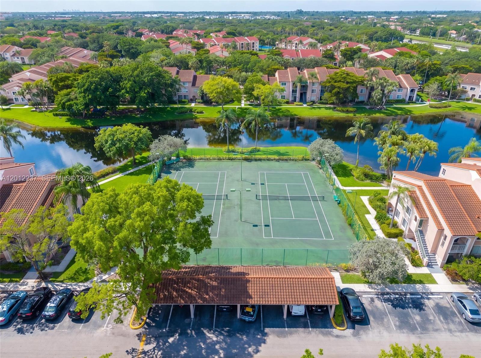 An aerial view shows two tennis courts situated between residential buildings and a lake — MIRAMAR, FL