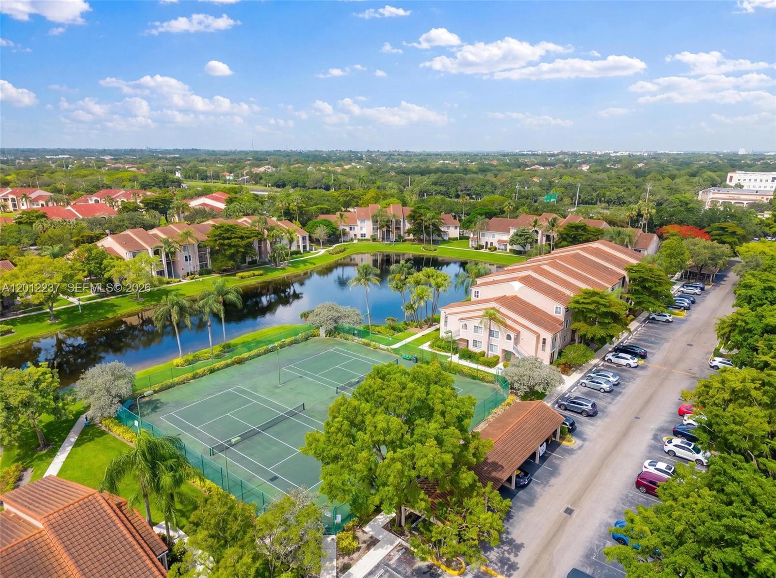 An aerial view shows apartment buildings, a tennis court, a pond, and a parking lot — MIRAMAR, FL