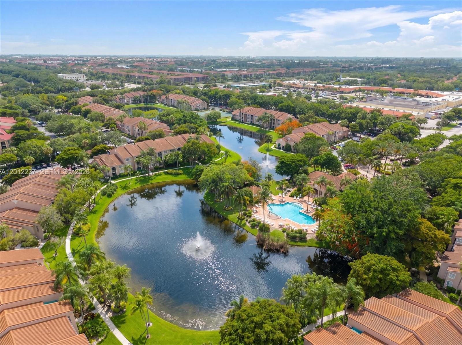 An aerial view shows a residential complex with multiple buildings, a lake with fountains, and a pool — MIRAMAR, FL