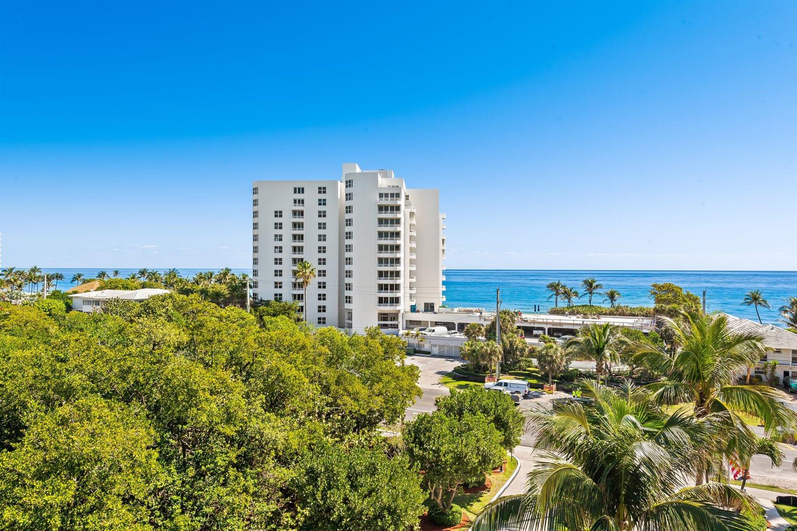 An exterior view of a white high-rise apartment building overlooking the ocean and trees — 3450 S Ocean Boulevard # 605, Highland Beach FL 33487, HIGHLAND BEACH, FL