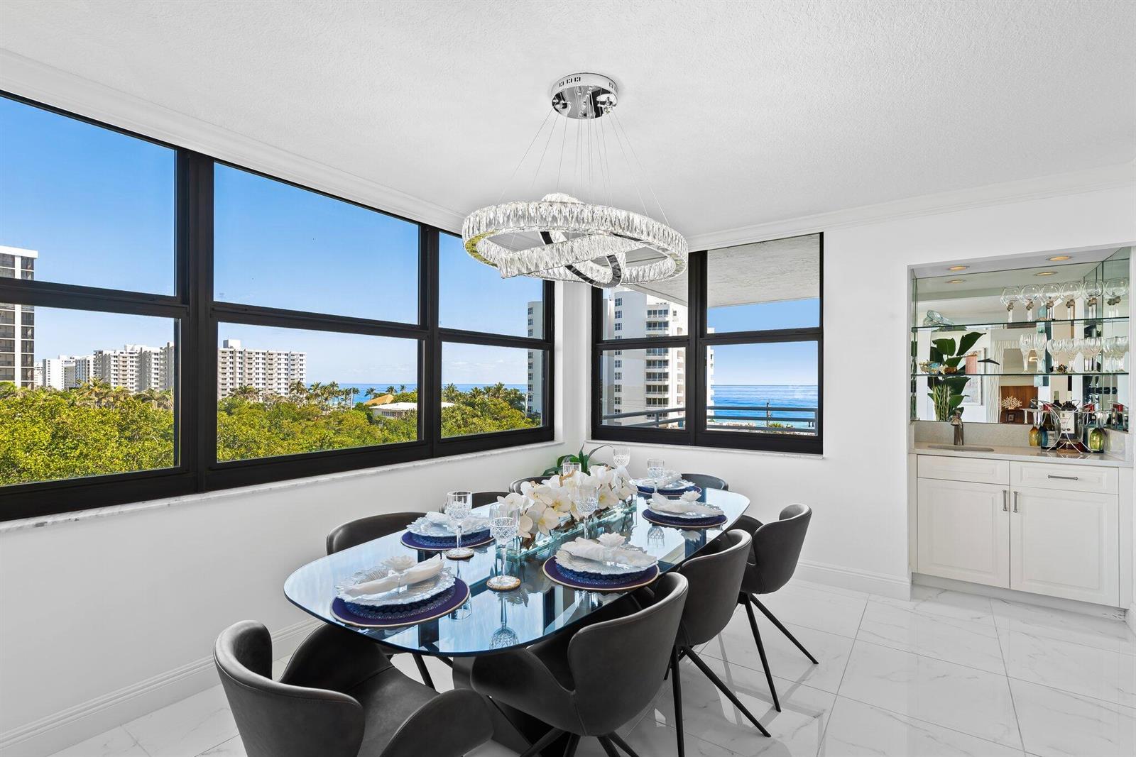 A dining room with a glass table, modern chandelier, and floor-to-ceiling windows overlooking the ocean — 3450 S Ocean Boulevard # 605, Highland Beach FL 33487, HIGHLAND BEACH, FL