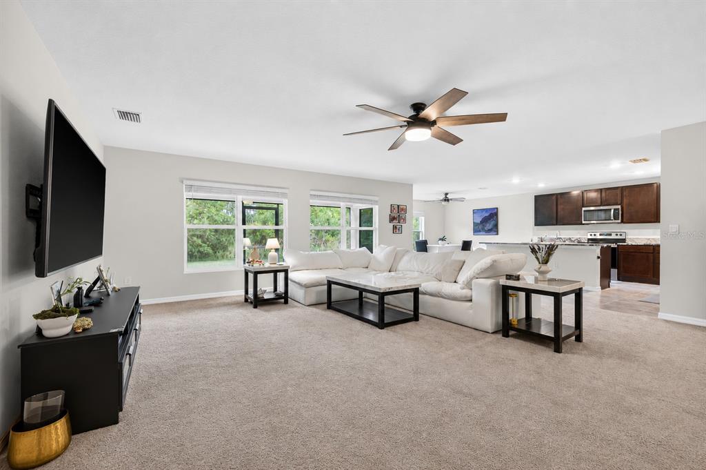 A spacious living room with beige carpeting, a white sectional sofa, and an open kitchen — 5442 DIANTHA WAY, BROOKSVILLE, FL