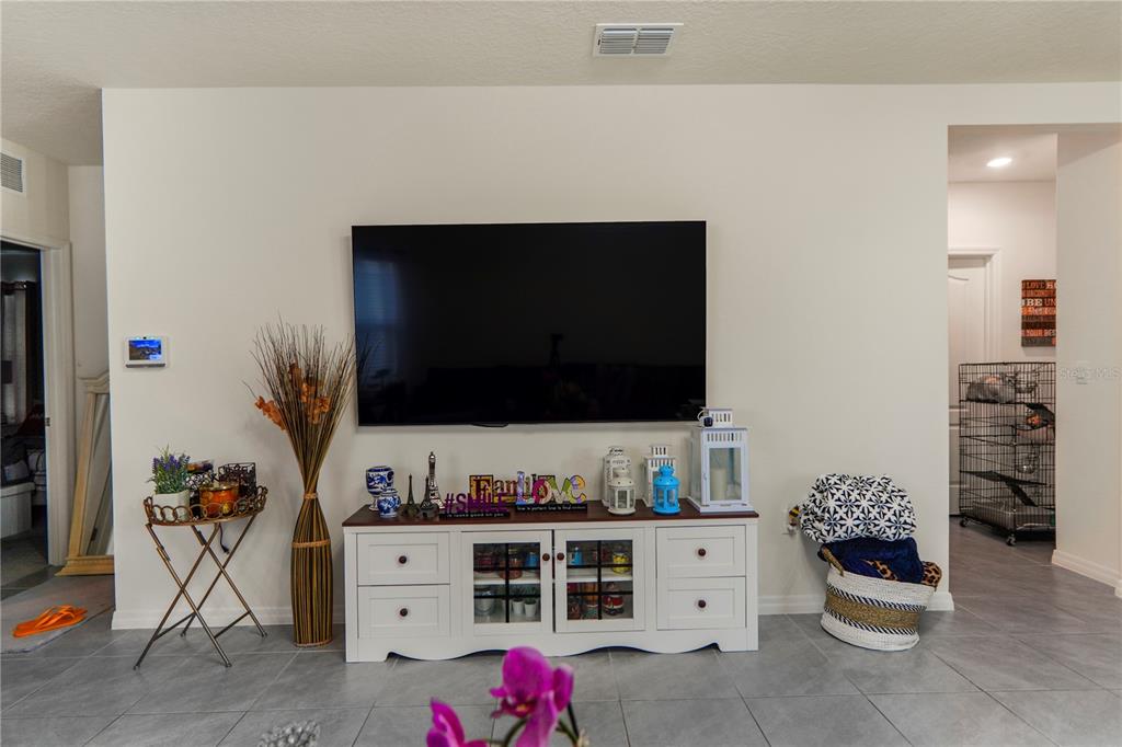 A living room features a wall-mounted television above a white media console and tile flooring — 2606 ANGEL FALLS DRIVE, DAVENPORT, FL