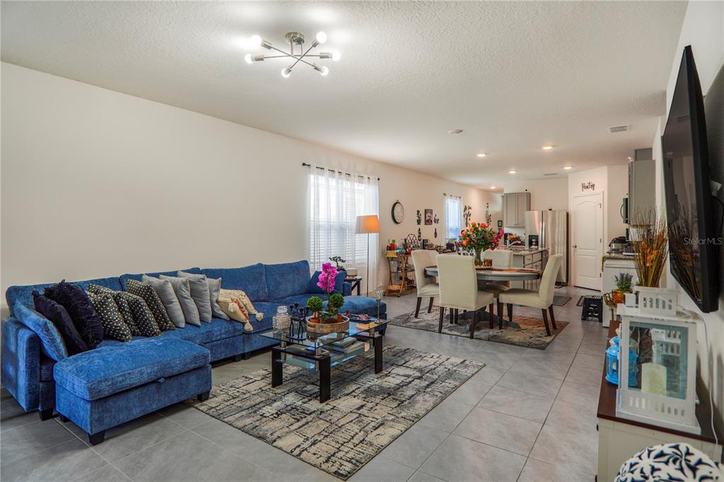 An open-concept living and dining area features a blue sectional sofa, tile flooring, and kitchen — 2606 ANGEL FALLS DRIVE, DAVENPORT, FL