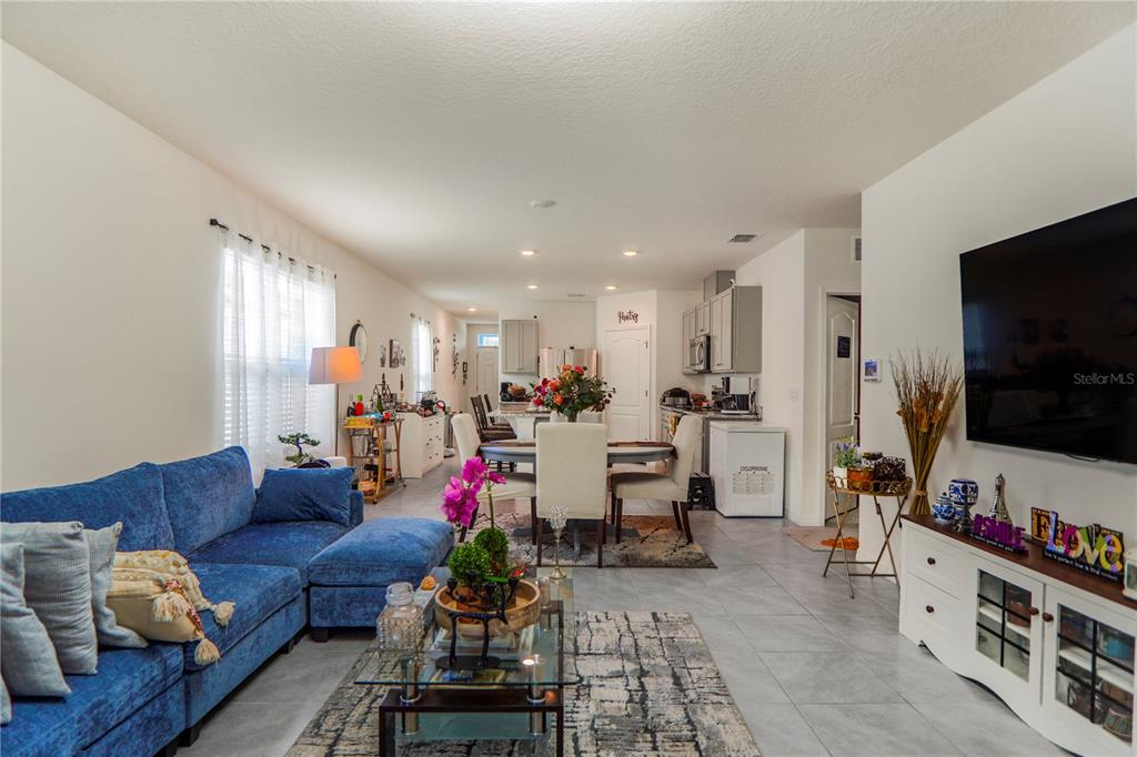An open-concept living and dining area features a blue sectional sofa, tile floors, and kitchen — 2606 ANGEL FALLS DRIVE, DAVENPORT, FL