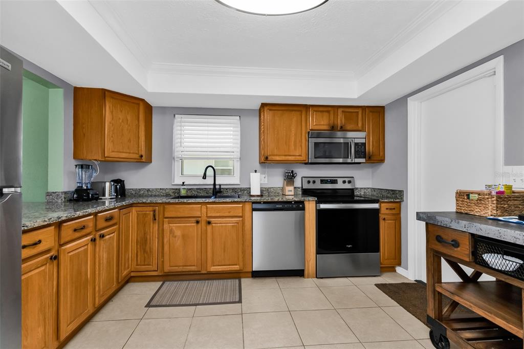 A kitchen features wood cabinets, granite countertops, stainless steel appliances, and light-colored tile flooring — 82 ROTONDA CIRCLE, ROTONDA WEST, FL