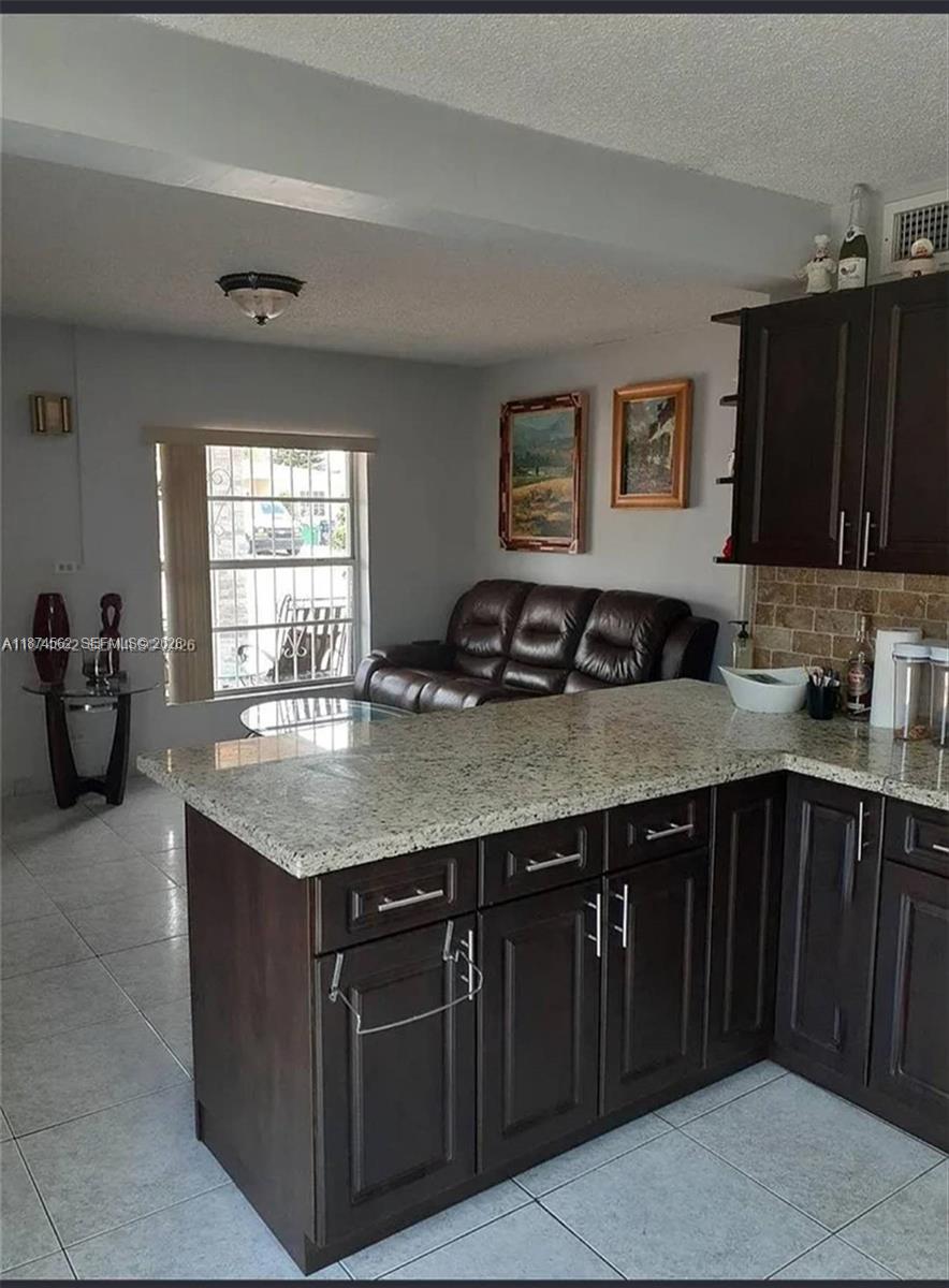 A kitchen with granite countertops and dark wood cabinets overlooks a living area with seating — 9360 SW 37th St, Miami FL 33165, MIAMI, FL