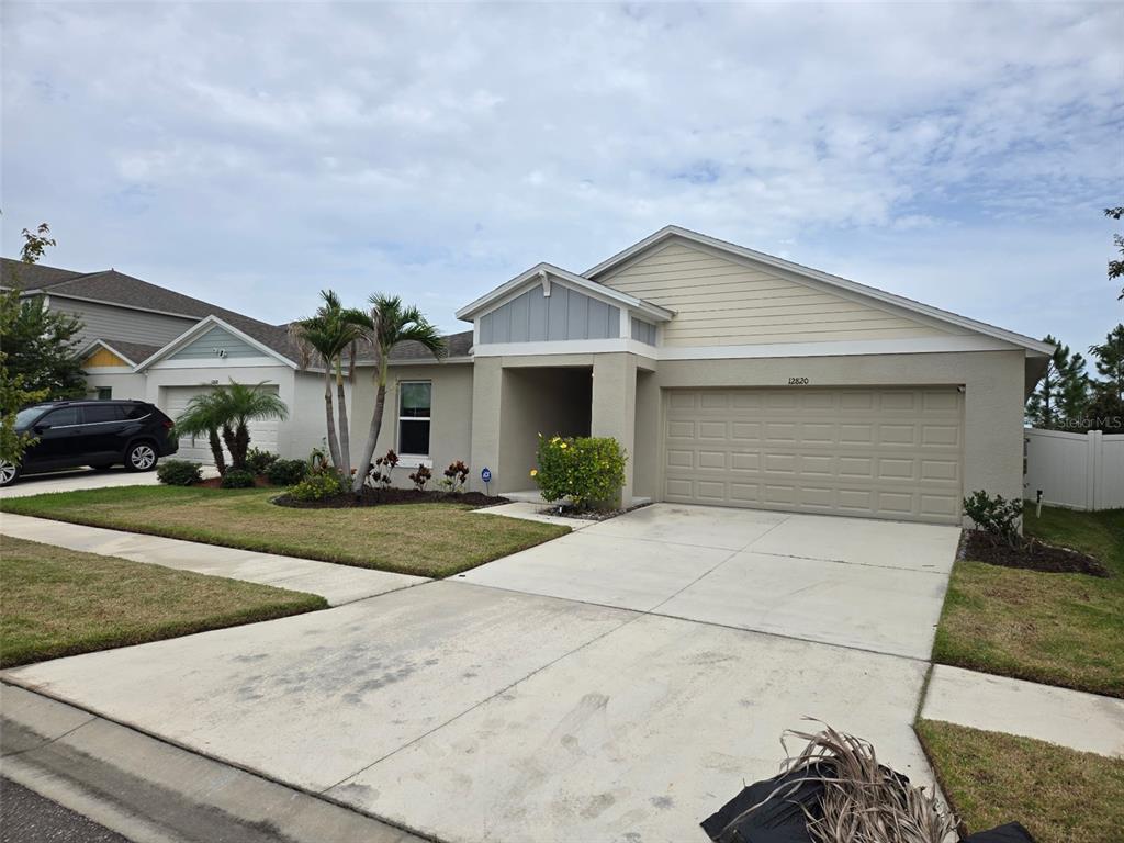 A single-story suburban house with a beige stucco exterior, a two-car garage, and palm trees — 12820 BENT TWIG DRIVE, RIVERVIEW, FL