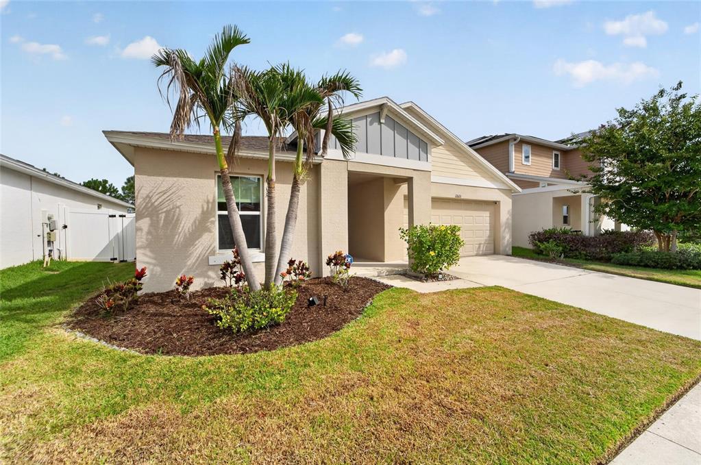 A single-story suburban house with a tan stucco exterior, a two-car garage, and palm trees — 12820 BENT TWIG DRIVE, RIVERVIEW, FL