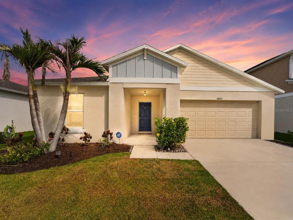 A single-story suburban house with a beige stucco exterior, a two-car garage, and palm trees — 12820 BENT TWIG DRIVE, RIVERVIEW, FL