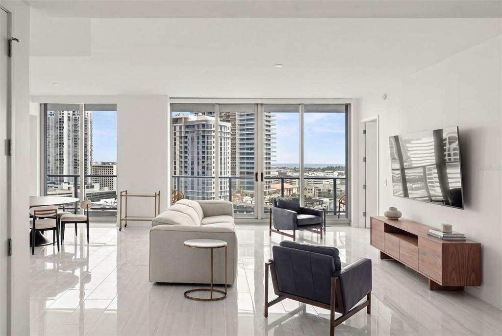 A modern living room features white tile floors, a light sofa, two dark chairs, and floor-to-ceiling windows — 400 CENTRAL AVENUE UNIT 1405, ST PETERSBURG, FL