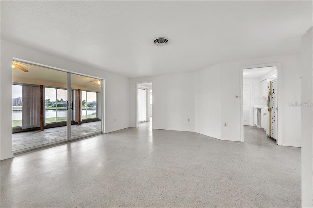 A bright, empty living room features white walls, polished concrete floors, and sliding glass doors — 3395 PINETREE STREET, PORT CHARLOTTE, FL