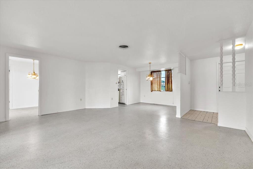 An open-concept living and dining area features white walls, light-colored flooring, and two chandeliers — 3395 PINETREE STREET, PORT CHARLOTTE, FL
