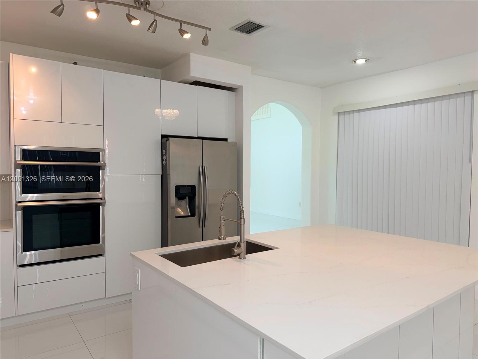 A modern kitchen features white glossy cabinets, a stainless steel refrigerator, and a central island — 3802 SW 165th Ter # 0, Miramar FL 33027, MIRAMAR, FL