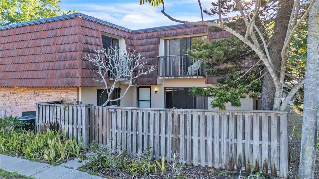 A two-story townhouse with a brown mansard roof, wooden privacy fence, and a small balcony — 2605 10TH COURT, PALM HARBOR, FL