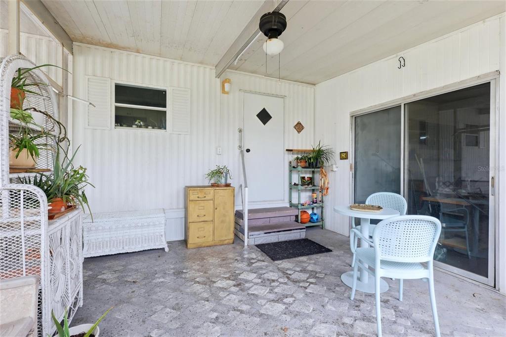 A covered patio features a white door, sliding glass doors, and a small bistro set — 6710 36TH AVENUE E UNIT 197, PALMETTO, FL
