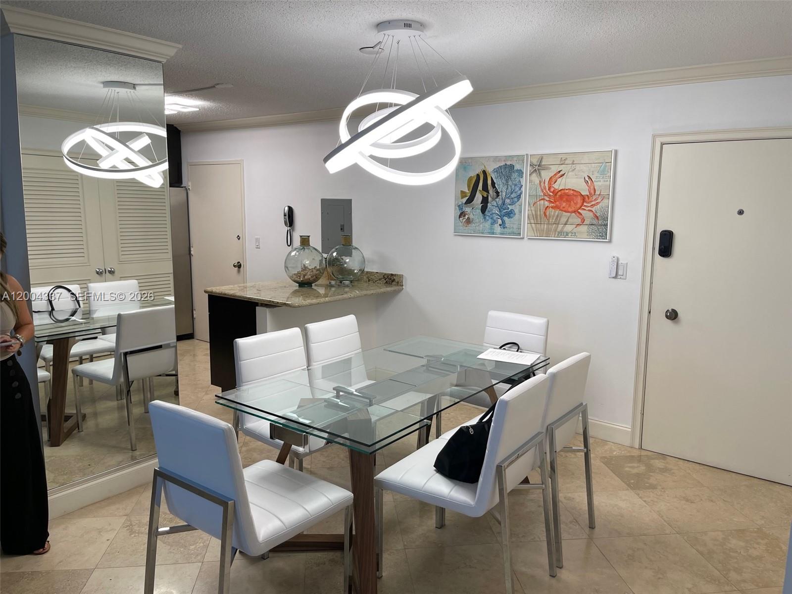 A dining room features a glass table, white chairs, and a modern circular light fixture — 5555 Collins Ave # 7Z, Miami Beach FL 33140, MIAMI BEACH, FL