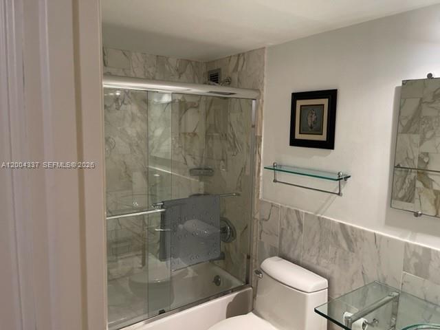 A bathroom features a glass-enclosed shower with marble tile walls and a white toilet — 5555 Collins Ave # 7Z, Miami Beach FL 33140, MIAMI BEACH, FL