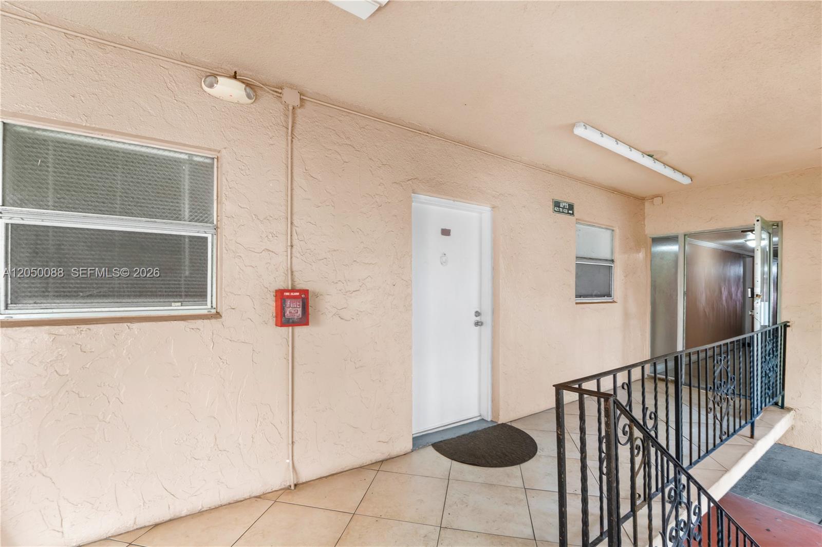 An exterior apartment hallway features a white door, a fire alarm, and metal railings — 1305 W 53rd St # 420, Hialeah FL 33012, HIALEAH, FL