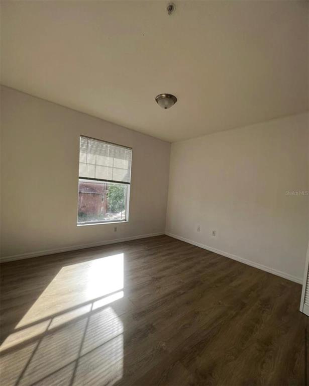 An empty bedroom features light wood-look flooring, white walls, a single window, and a ceiling light — 5548 METROWEST BOULEVARD UNIT 306, ORLANDO, FL